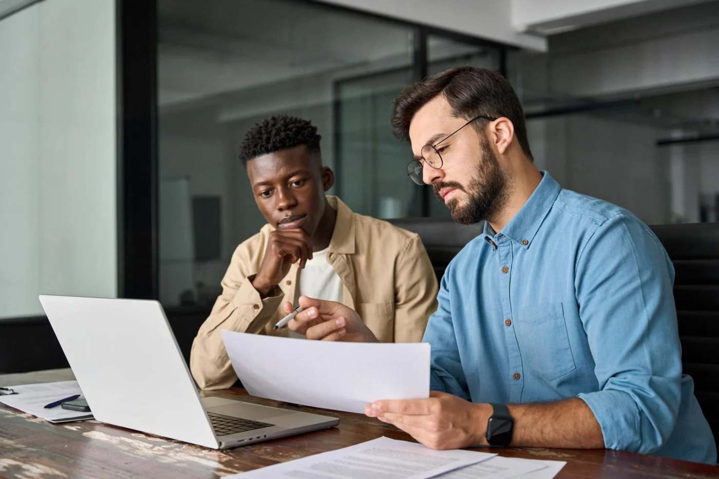Two colleagues discussing printed financial reports in a modern office