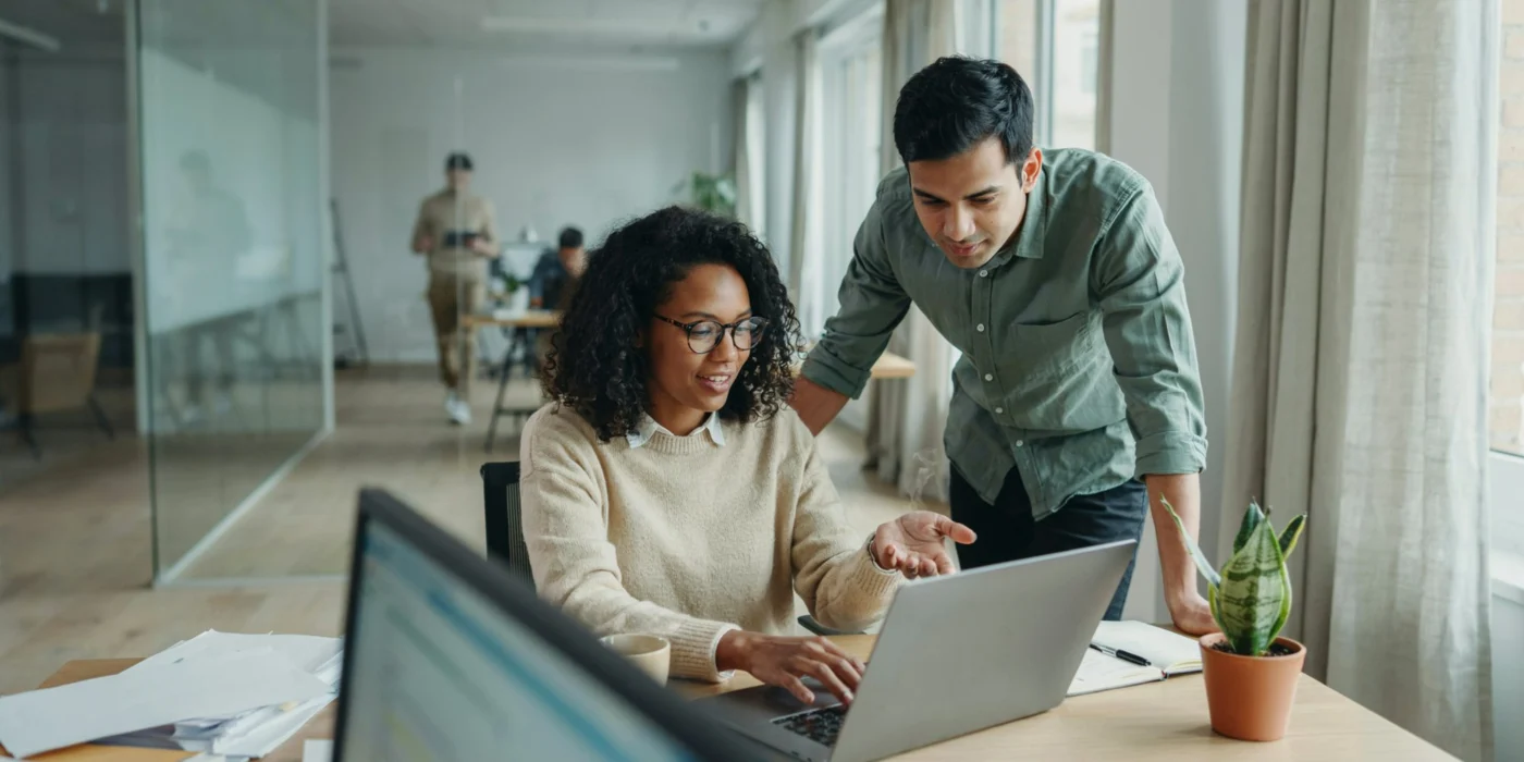 Two colleagues reviewing figures together on a laptop in a modern office