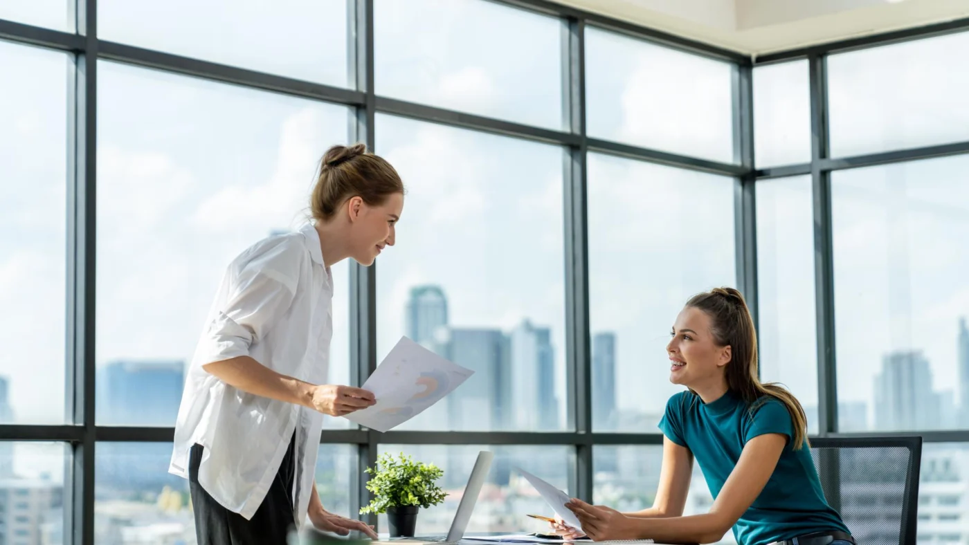 Two colleagues review a document together in a bright glass office