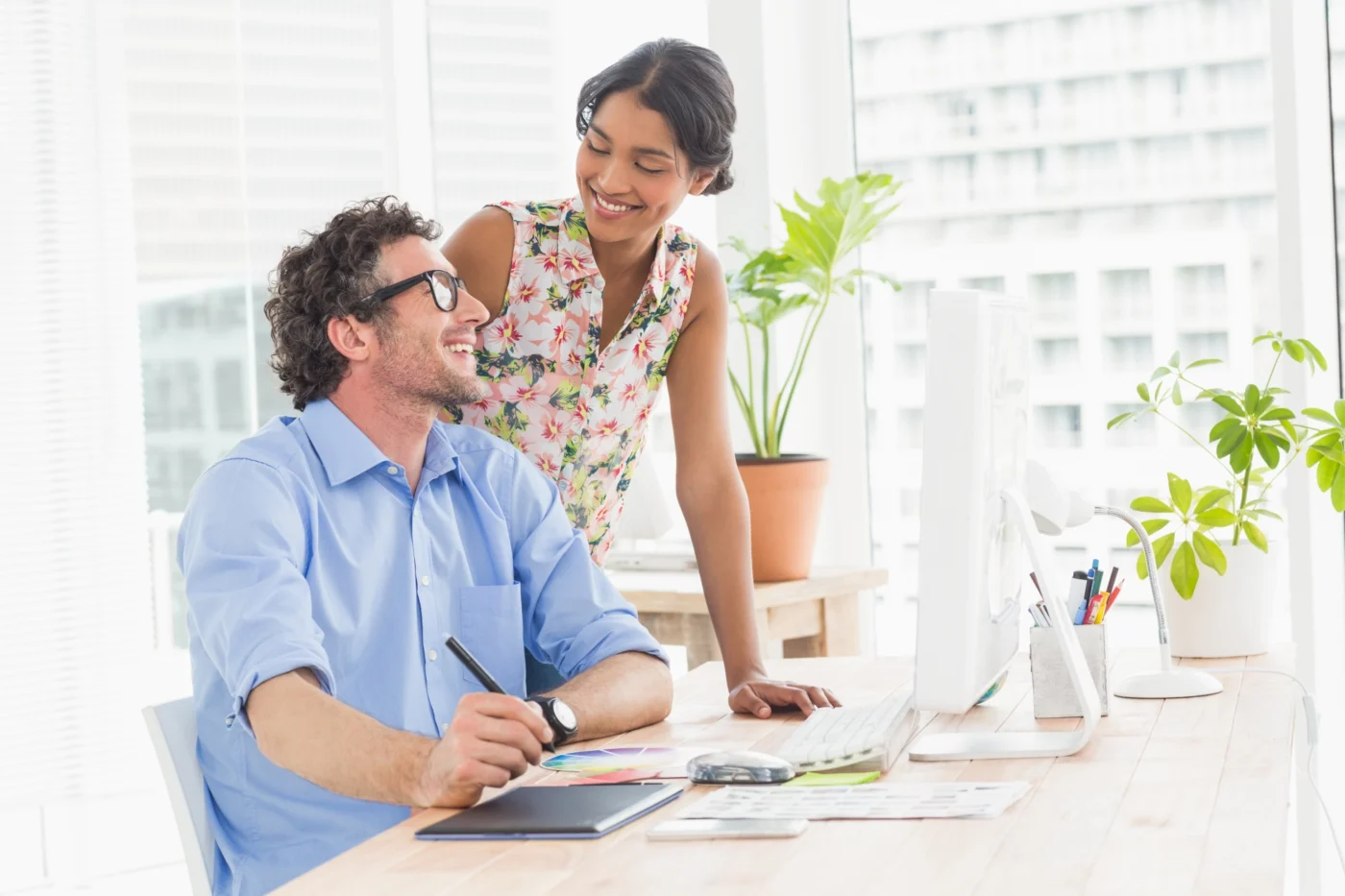 A colleague points out a figure on screen while another looks on at a standing desk