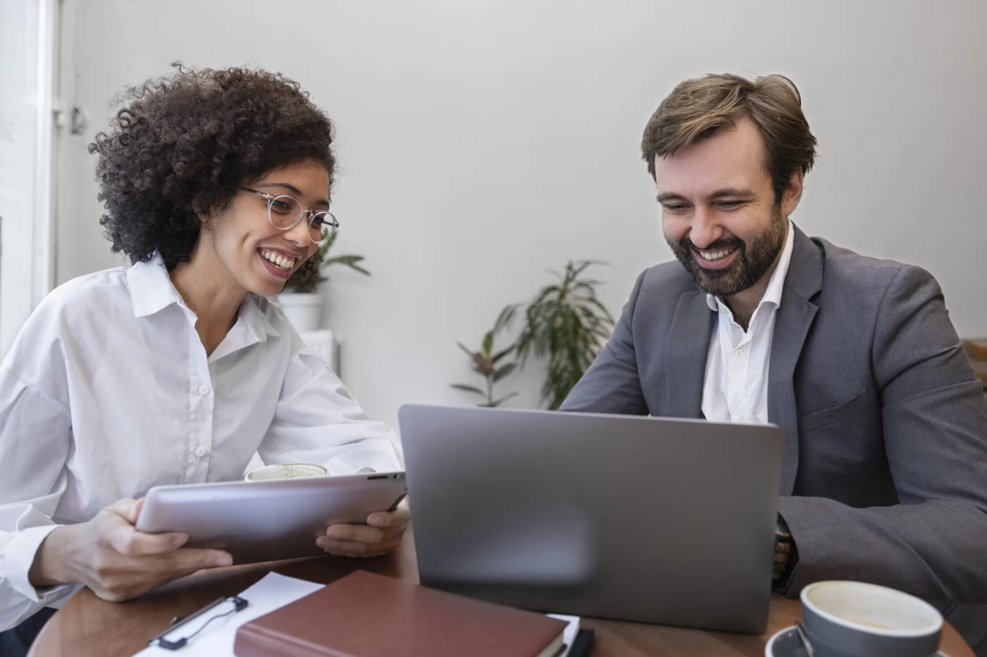 A colleague and client compare figures on a laptop, smiling