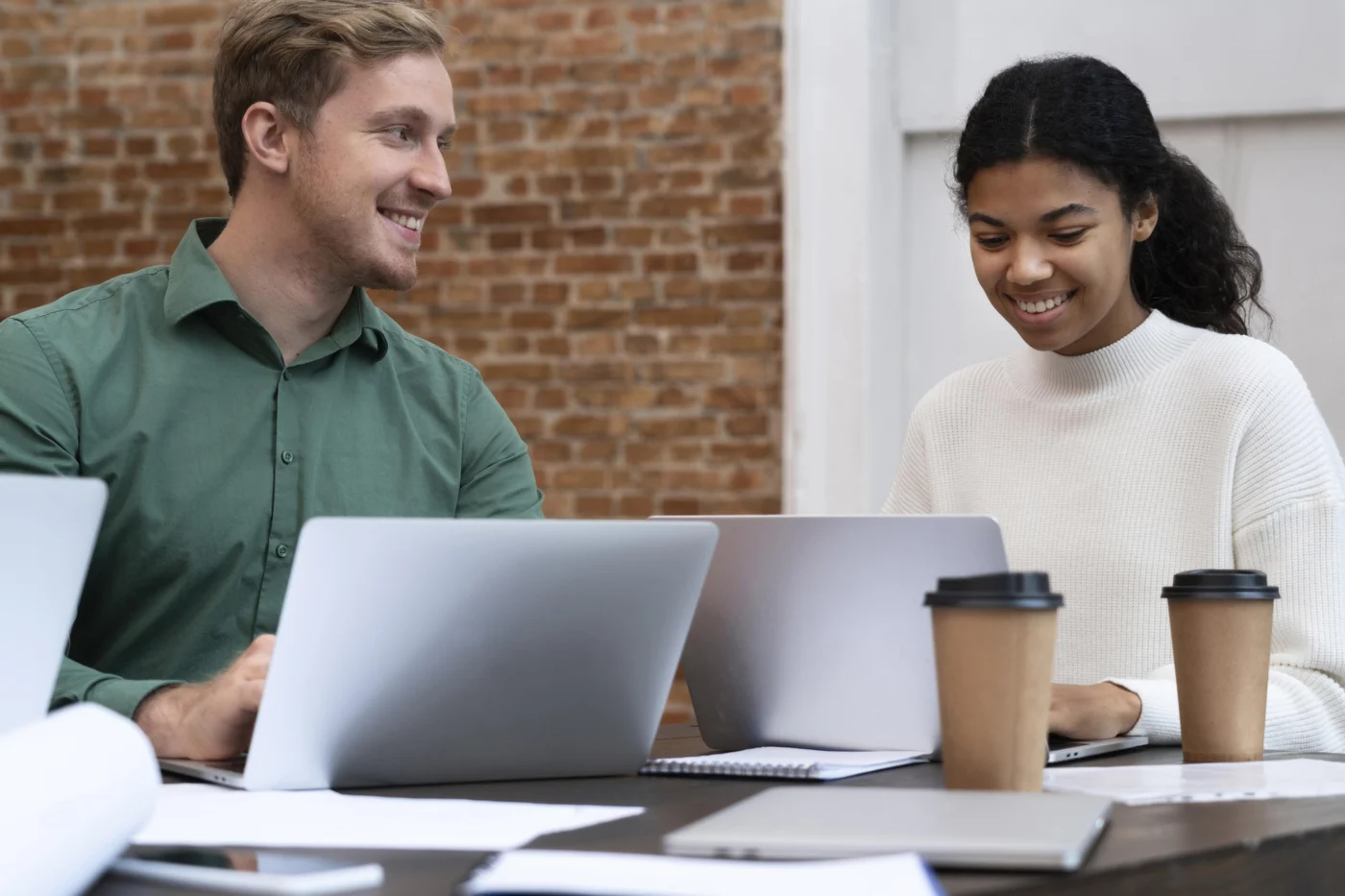 Two colleagues check a working pattern together over coffee and a laptop