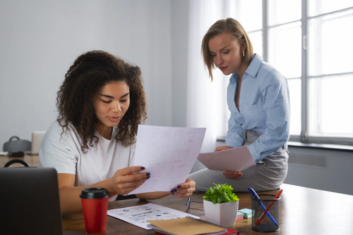 A colleague points out a figure on a payslip to another at a plant-filled desk