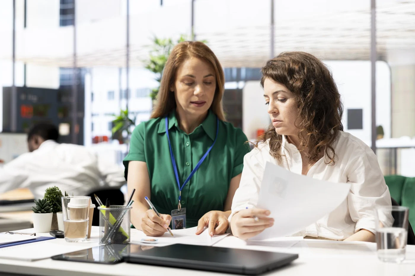 A colleague reviews an employee's contract with another at a city-view desk