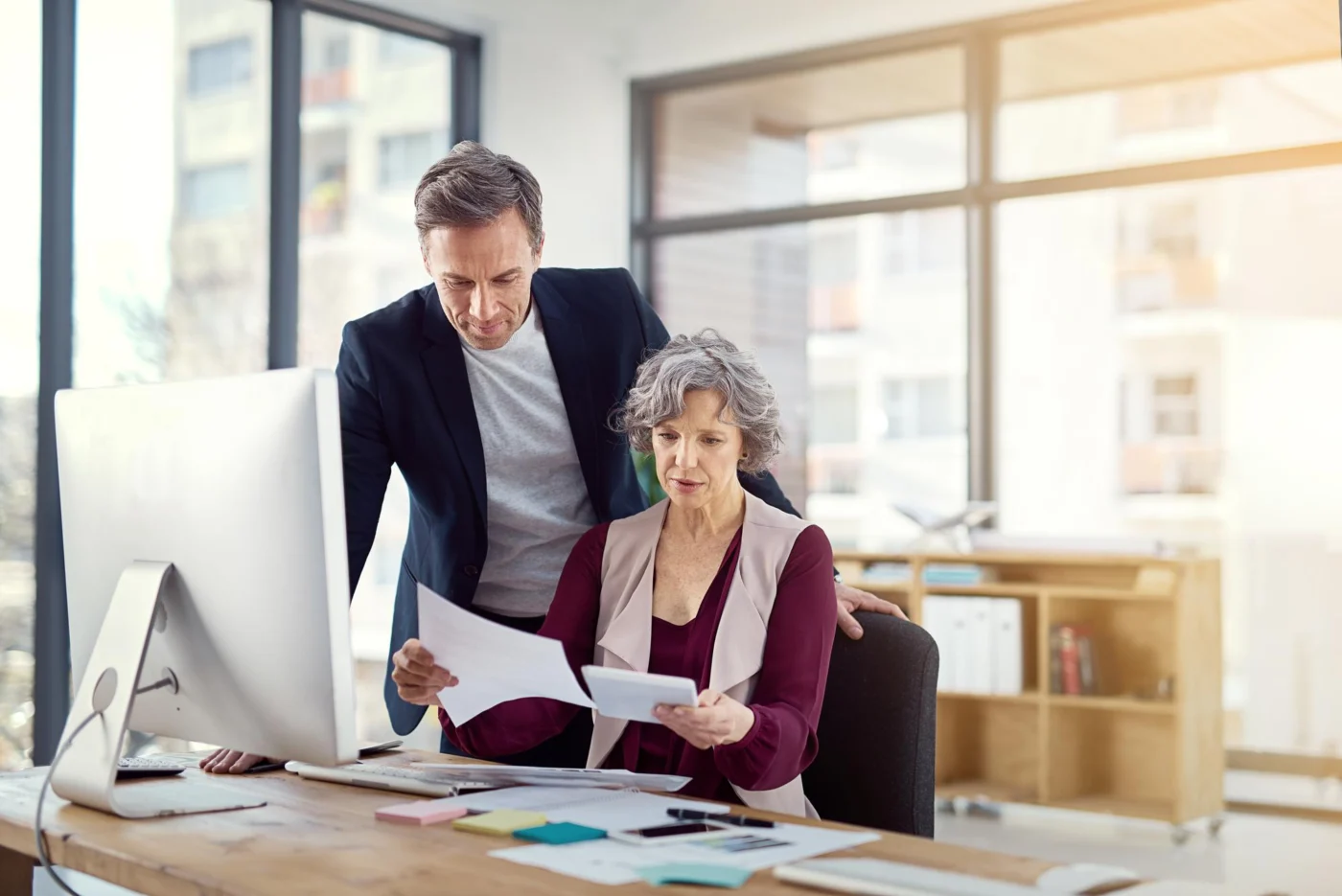A colleague and a senior client review documents together at a desk