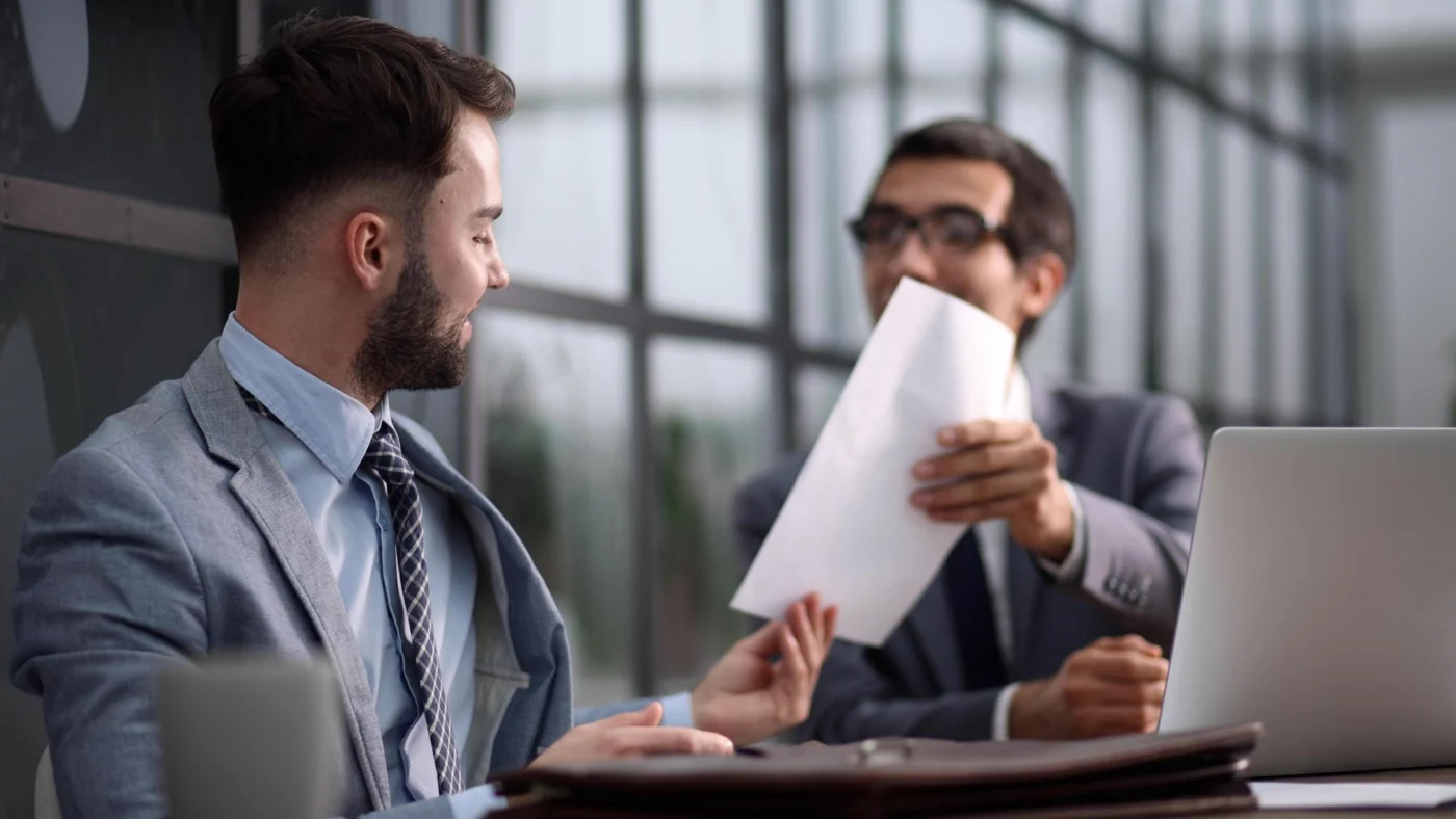 Two colleagues look over a document on a laptop screen at a desk